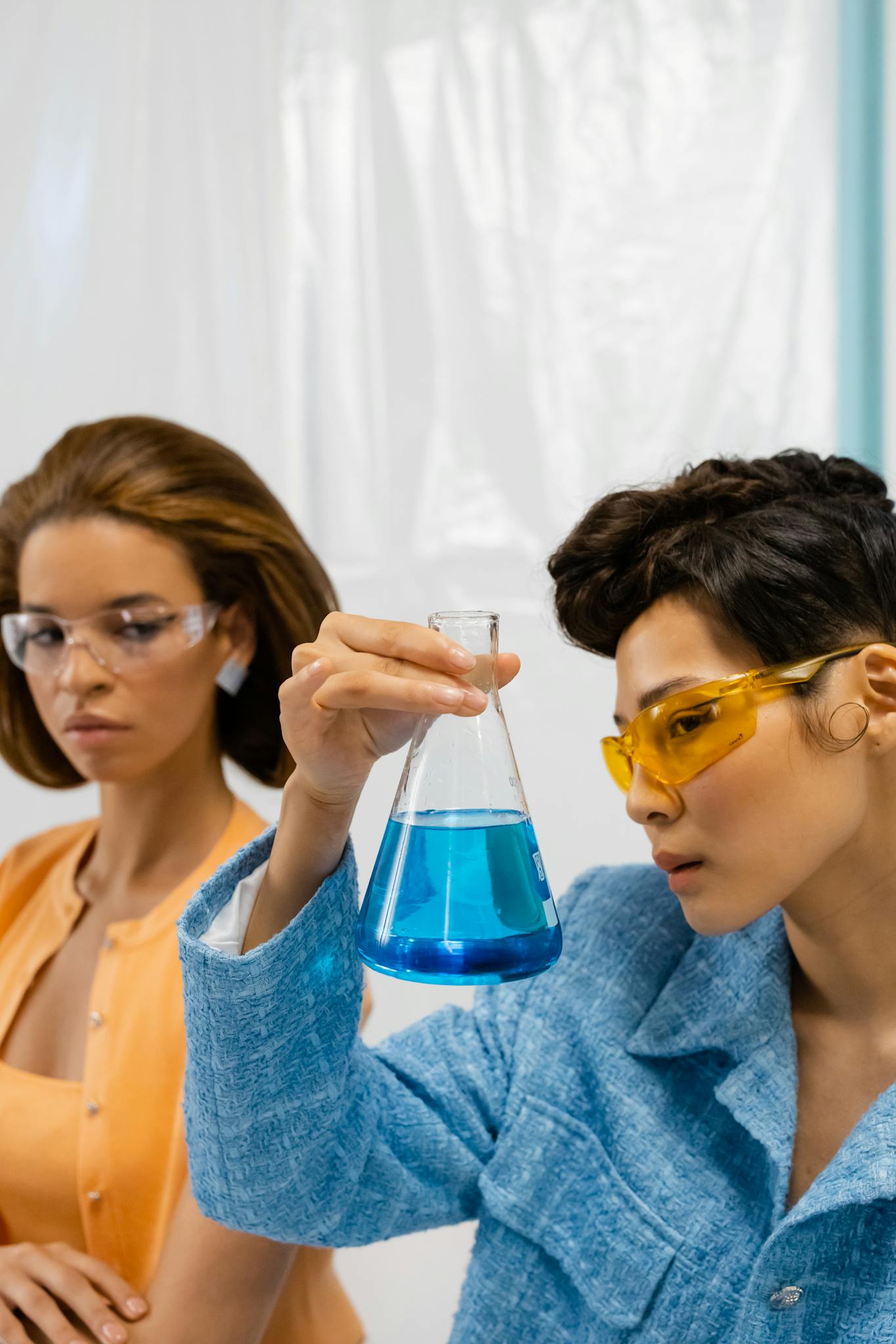 Two female scientists examining a flask with blue liquid in a laboratory setting.